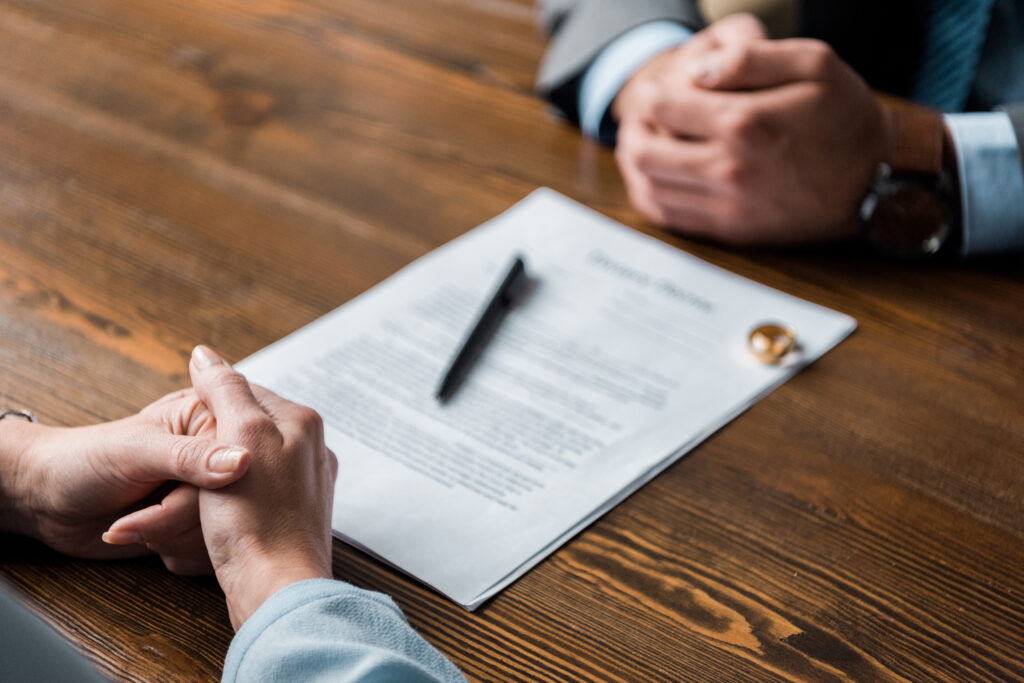 Two people seated at a wooden table with hands clasped near a document and pen. The document's heading reads "Divorce Papers," underscoring the expertise of Huntersville Family Law Attorneys in navigating such challenging situations.