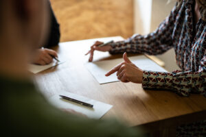 People seated at a wooden table reviewing documents, with pens and papers laid out in front of them. A person, possibly one of the Denver Workers Compensation Attorneys, is pointing to a paper, discussing its content.