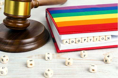 Judge gavel with word Adoption in wooden blocks in notebook and rainbow LGBT flag, LBGT Family law
