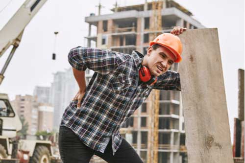Young construction worker rubbing hurt back, most common workplace injuries