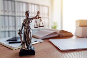 A statue of Lady Justice holding scales and a sword on a desk, with an open book, documents, and office supplies in the background, represents the steadfast dedication of a Huntersville Family Law Attorney.