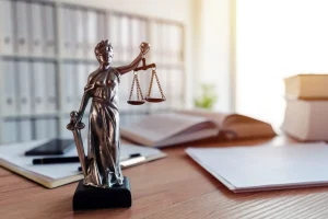 A statuette of Lady Justice holding scales and a sword stands on a desk with books, papers, and office supplies in the background, symbolizing fairness in Workers' Compensation cases.