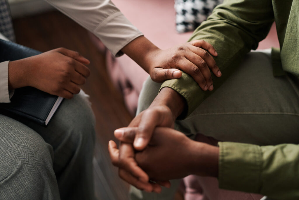 Two individuals holding hands, one person resting a hand on the other's arm. One holds a black notebook, perhaps seeking advice from a Denver divorce Attorney.