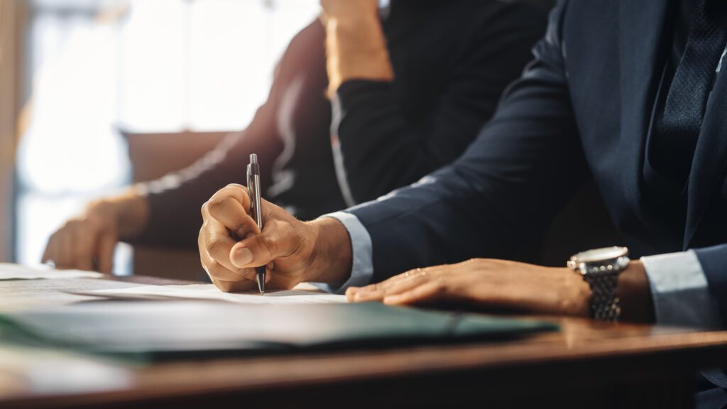 A person in a suit writes on a document at a desk, with another individual seated beside them in the background—clear signs of collaboration often seen with Charlotte Family Lawyers.