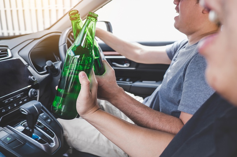 Two men in a car drinking alcohol. This is illegal, and could be indicative of an alcohol abuse problem.