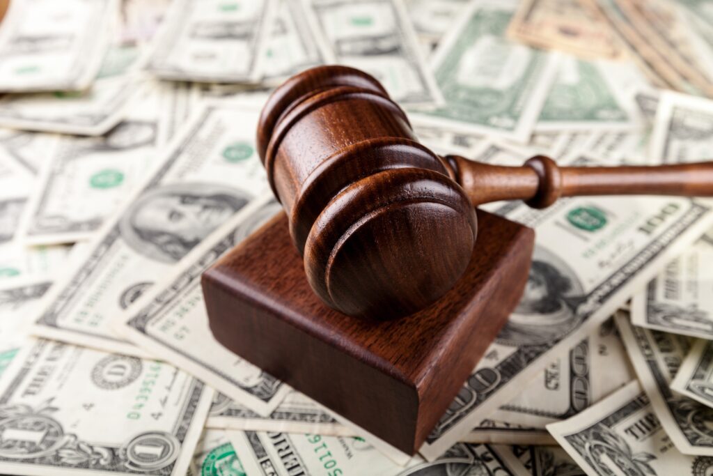 A wooden gavel rests on its block atop a pile of US dollar bills, evoking the poignant decisions often seen in the office of a judge.