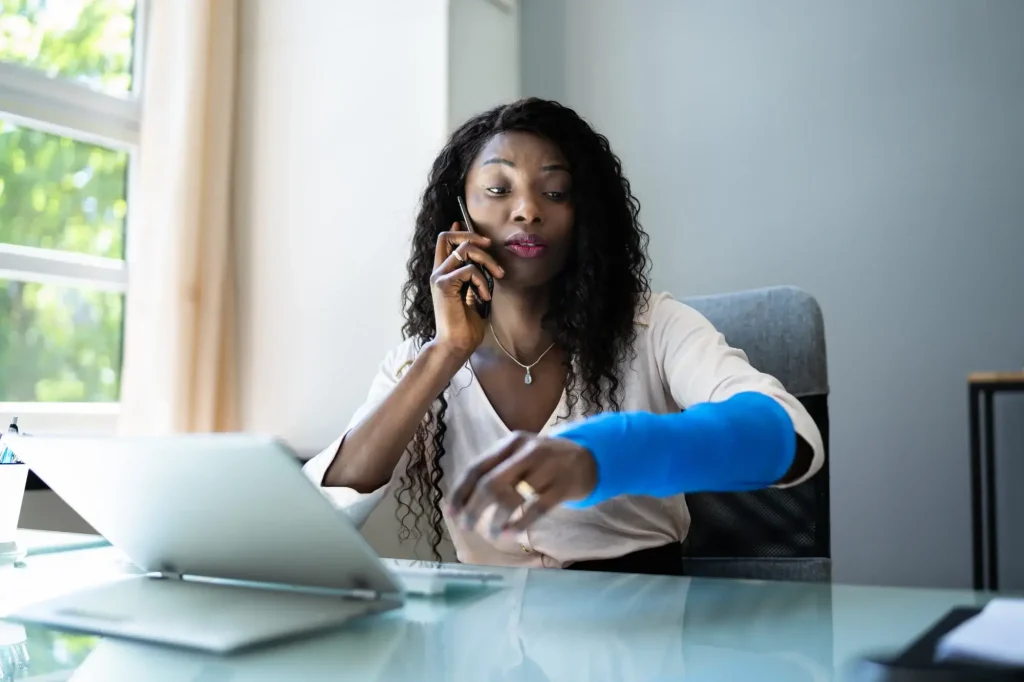Injured employee with an arm cast speaking on the phone while managing a workers’ compensation claim from home.