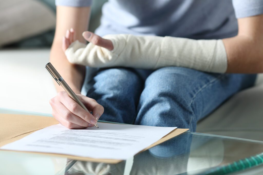 Injured worker with an arm cast signing workers’ compensation claim paperwork after a workplace accident.