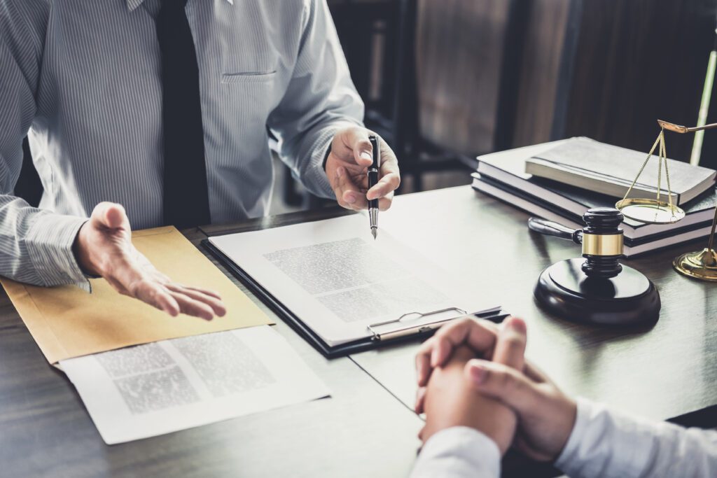 Two people are seated at a desk with legal documents, a gavel, and scales of justice.