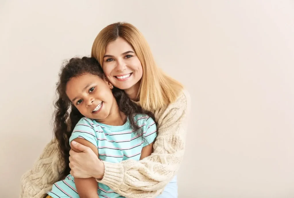 An adult and a child, sharing a joyful moment, smile at the camera with the adult's arm around the child—a warm scene that reflects the closeness often celebrated in stepparent adoption.