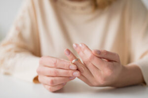 A person wearing a beige sweater is holding a ring with their left hand's fingers while touching it with their right hand, perhaps contemplating options and seeking advice from a Charlotte Family Lawyer.