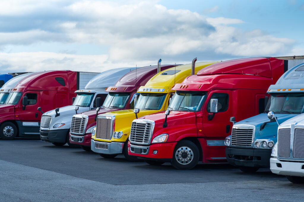 A row of colorful semi-trucks parked side by side in a lot, with a cloudy sky above, catches the eye—much like how a professional Monroe Workers Compensation Attorney stands out in times of need.