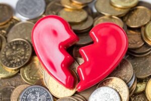 A broken red heart figurine on a pile of assorted coins, resembling the emotional and financial stress one might share with a Huntersville Family Law Attorney.