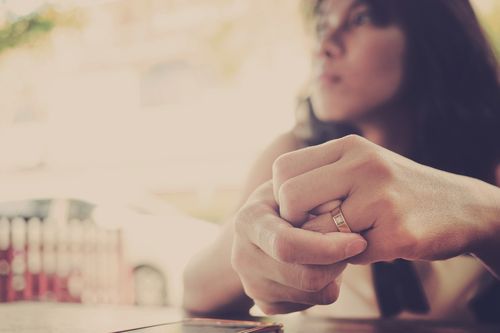 A person wearing a ring on their left hand clasps their hands together while sitting at a table; their face slightly out of focus in the background, resembling a client consultation with a Monroe Workers Compensation Attorney.