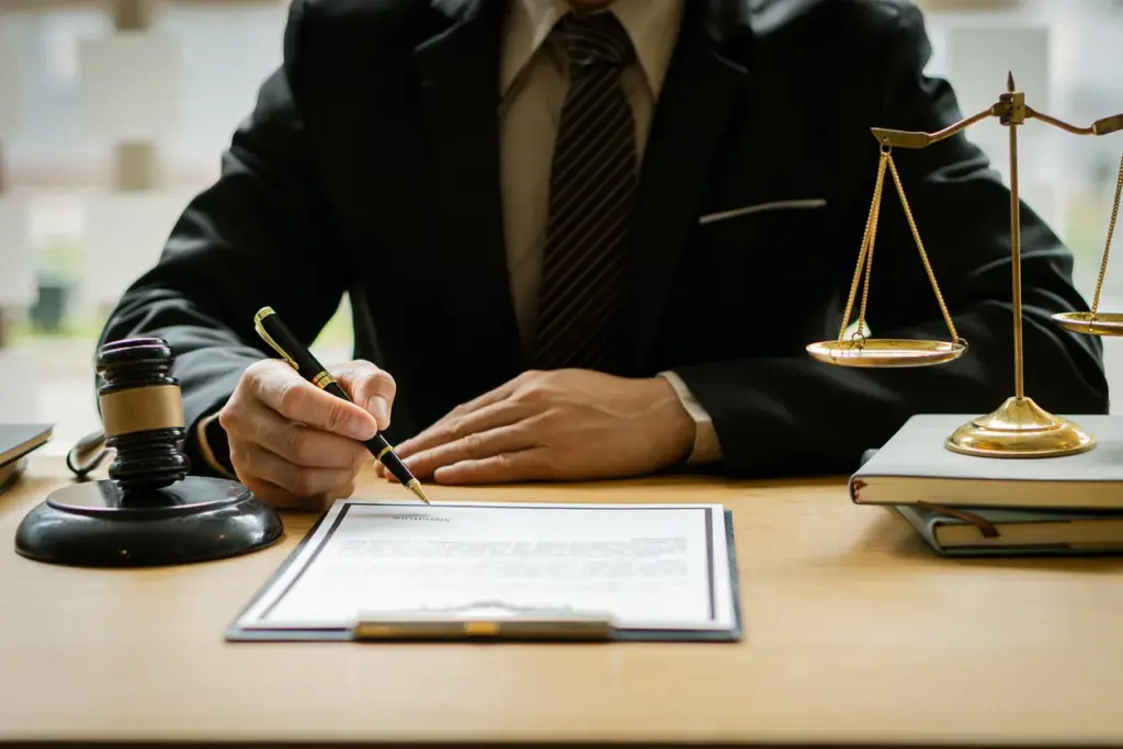 A person in a suit, likely a Monroe Workers Compensation Attorney, signs a document at a desk adorned with a gavel and scales of justice.