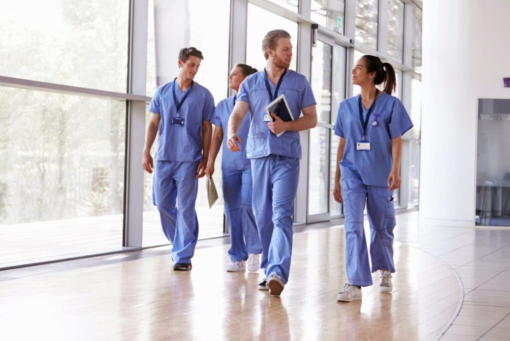 A group of five healthcare professionals in scrubs walk through a well-lit hallway with large windows, engaged in conversation, reminiscent of how Denver Workers Compensation Attorneys might collaborate to ensure client well-being.