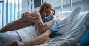 In the Hospital, Happy Wife Visits Her Recovering Husband who is Lying on the Bed. They Lovingly Embrace and Smile.