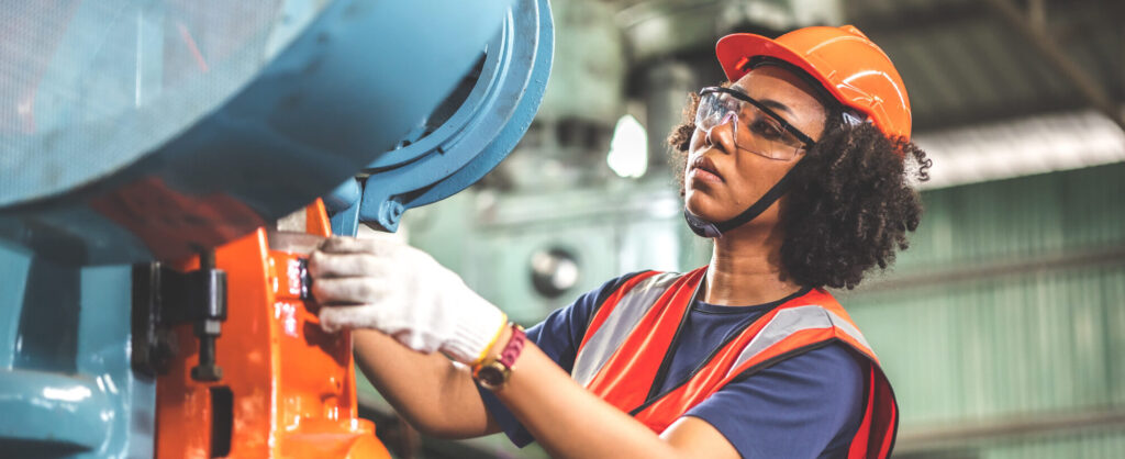 A person in a hard hat, safety goggles, and a high-visibility vest operates industrial machinery indoors—safety is paramount. If you or someone you know ever needs assistance with work-related injuries, consider reaching out to a Charlotte Workers Compensation Lawyer for dedicated support.