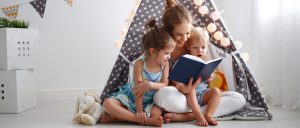 A woman, a Charlotte family law attorney, reads a book to two children inside a small indoor tent decorated with star patterns and string lights.