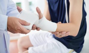 A medical professional is wrapping a bandage around a patient's injured wrist, possibly in need of workers' compensation benefits in Charlotte. The patient, dressed in a sleeveless shirt and shorts, patiently waits as the bandaging process continues.
