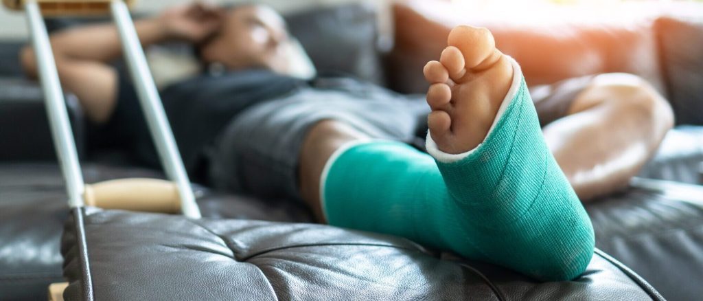 Person with a green leg cast resting on a couch, with crutches beside them, likely recovering from compensable injuries.