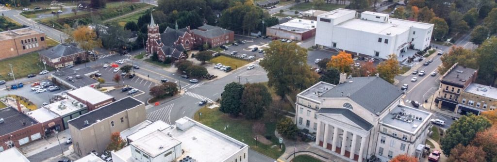 Aerial view of a town with a central large gray building, white building, roads, cars, and scattered trees. Several smaller buildings and a church surround the area, creating a picturesque setting where even a Lincoln County divorce lawyer might find solace.