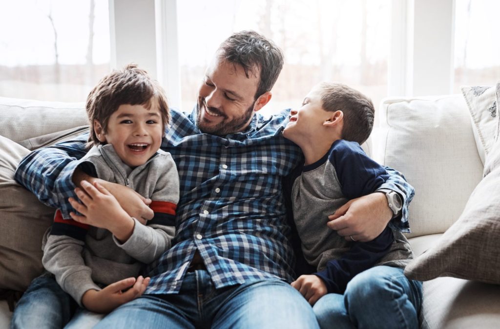 A dad with his 2 sons hugging on couch in home