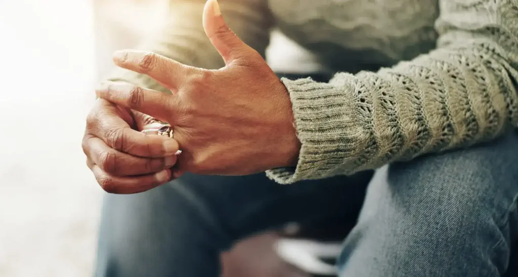 Close-up of a person wearing a green sweater and jeans, removing a ring from their left ring finger. This man is considering using the services of a Denver family law lawyer.