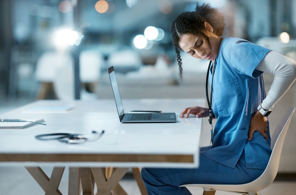 Healthcare worker experiencing lower back pain while working, a common cause of workers’ compensation claims.