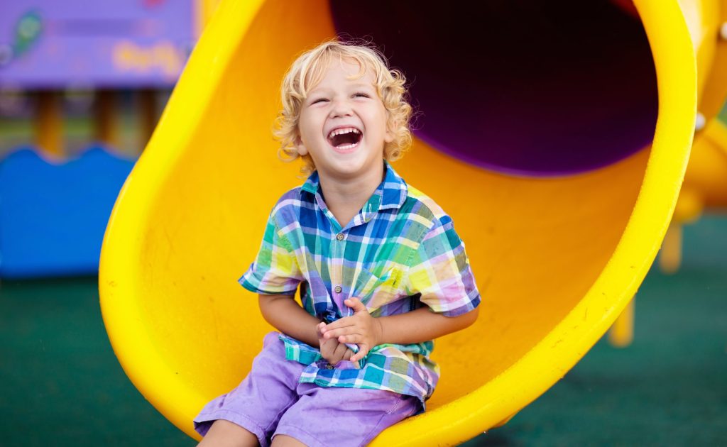 Young child laughing while playing on a playground slide, representing the child’s well-being and best interests in North Carolina custody and visitation proceedings.