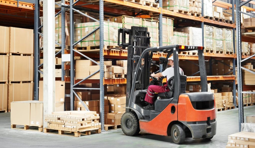 A person operates a forklift to move boxes in a large warehouse.