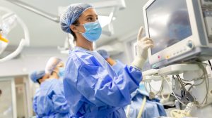 A medical professional in surgical scrubs and a mask operates a monitor in a hospital operating room, when needing workers comp attorney in Charlotte after work injury.