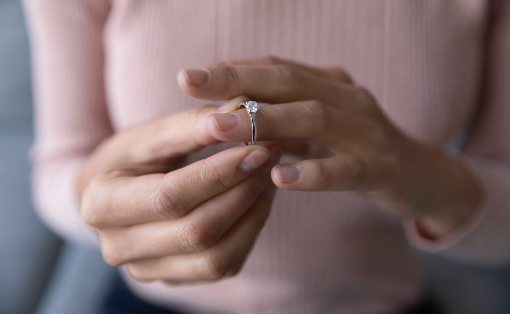 Woman removing wedding ring from finger as thinking divorce is coming and needing to consult with Charlotte high-asset divorce Lawyer.