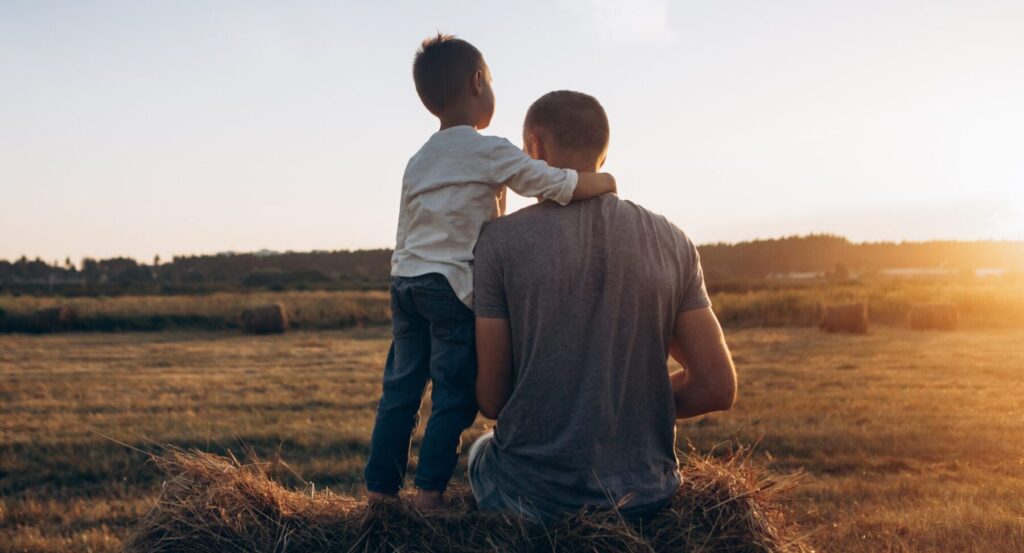 Small boy with father in a field at sunset.