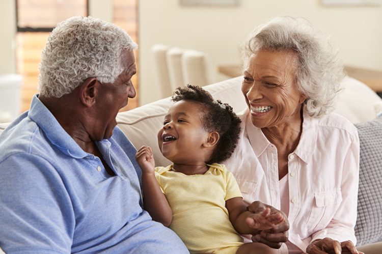 Grandparents smiling and spending time with their young grandchild on a couch, representing grandparent visitation and custody relationships in North Carolina family law cases.