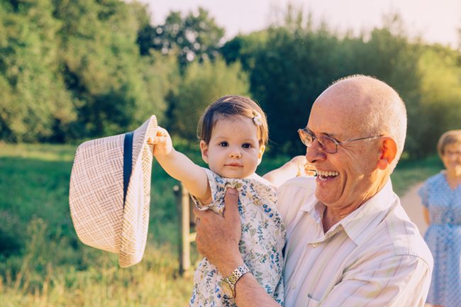 Grandfather holding a young child outdoors while smiling together in a field, representing the close emotional bond considered in North Carolina grandparent visitation disputes.