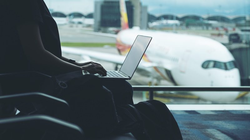Employee working on a laptop at an airport terminal during a business trip before a work-related flight.