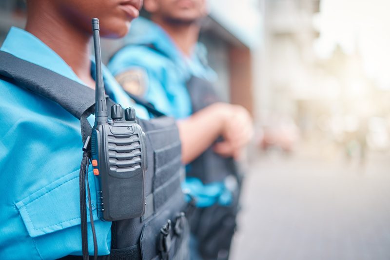 Radio, police and surveillance with a black woman officer standing outside while on patrol in the c.