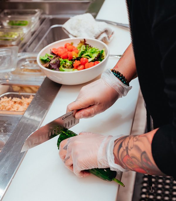 Line cook cutting a vegetable with sharp knife, representing the risk for cuts and lacerations for restaurant workers.