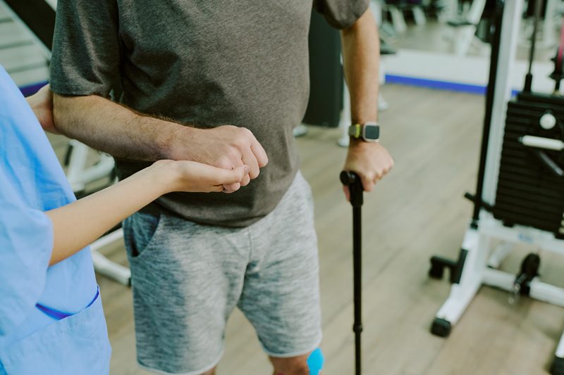 High angle shot of unrecognizable hand of doctor holding patients hand while they trying to walk together after serious knee injury