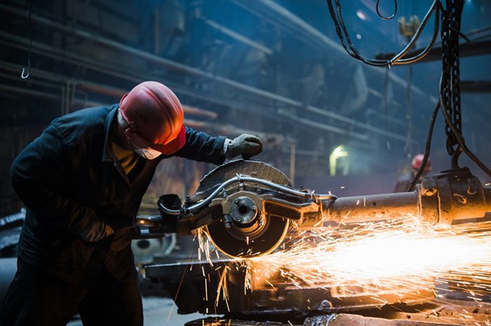 Welder used grinding stone on steel in factory with sparks.