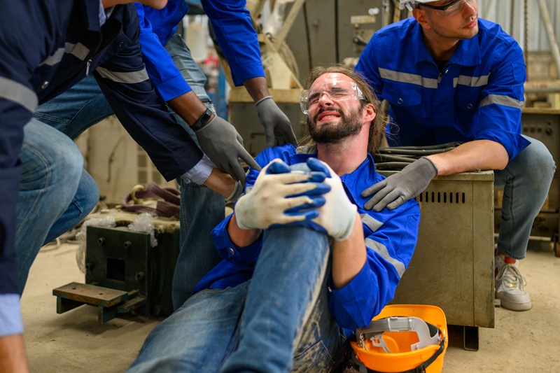 A worker clutching their leg after a work related injury. It could have been crushed under a piece of machinery.