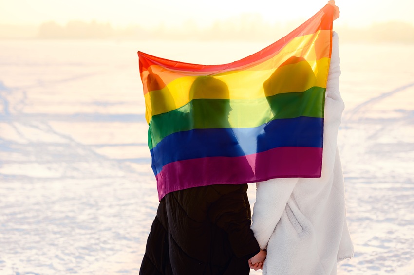 A same sex couple sits together with rainbow flag, looking out into the distance.