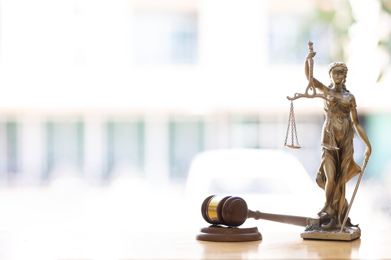 Lady Justice and a gavel sit on a desk in the bright sunlight of an office window.