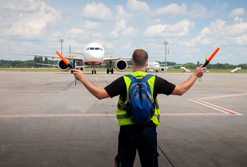 An airport worker using orange wands to direct the airplane on the runway.