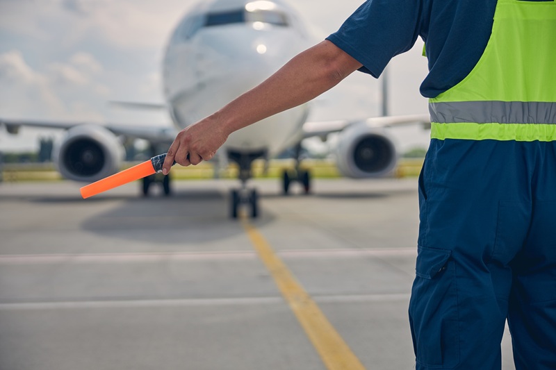 Cropped photo of an airport worker in uniform holding a marshaling wand in one hand
