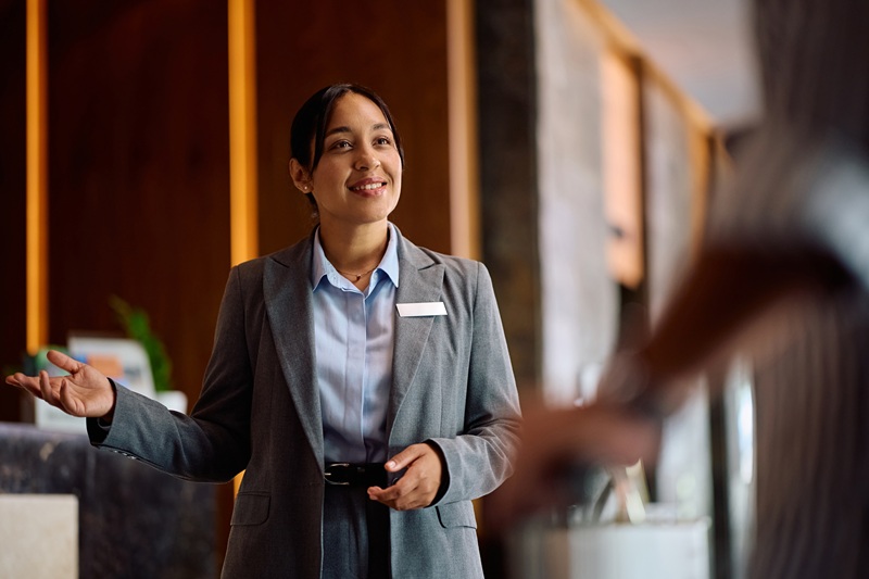 Happy female concierge welcoming a guest during check in at the hotel.