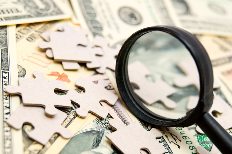 Money and puzzle pieces are scattered on a surface. There is a magnifying glass on top.