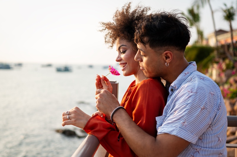 Happy romantic couple kissing on the beach at sunset. Diverse man and woman in love enjoy their summer vacation or date
