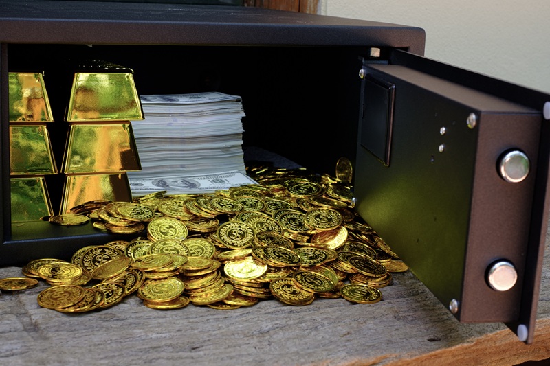 Steel safes box full of coins stack and gold bar and banknote 100 USD on the wooden table